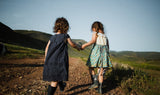 Two children happily holding hands, wearing playful outfits from a secondhand online thrift store, with a bright and cheerful background.
