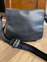 Gray leather bag with a black strap on a wooden surface

