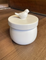 White ceramic container with a bird on top on a wooden floor

